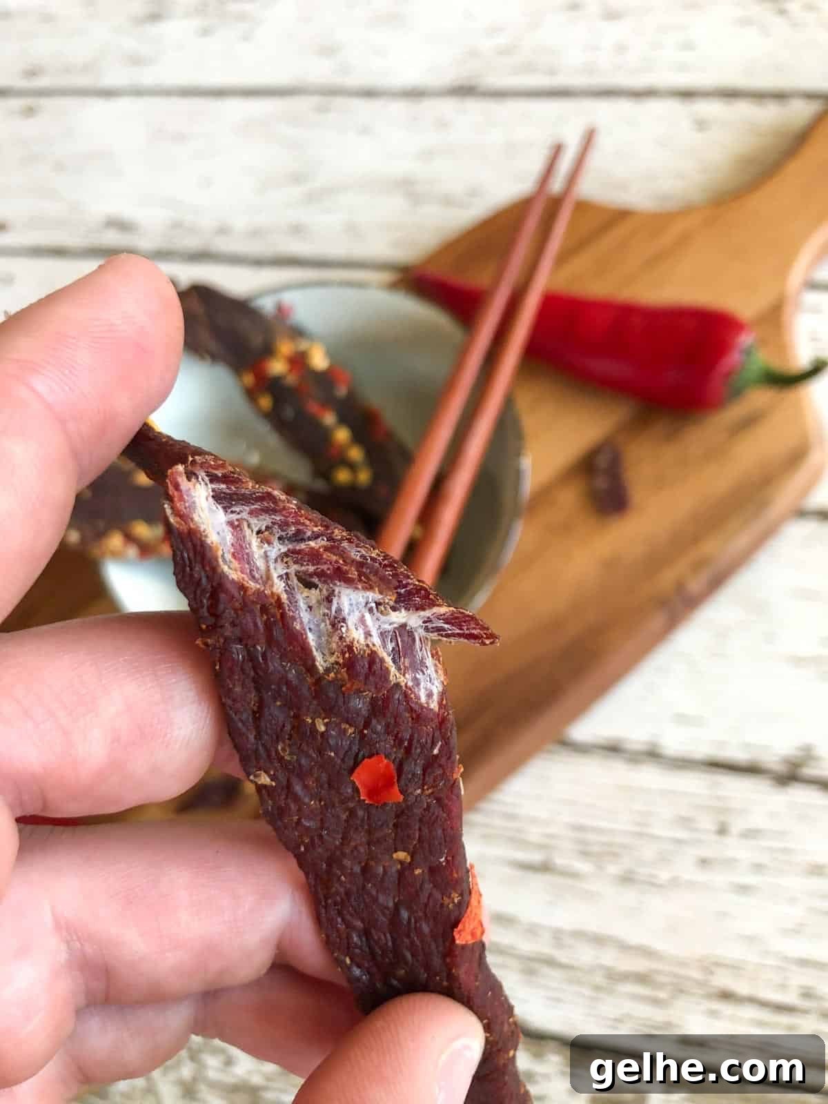 venison jerky bent in half showing it is finished drying by the white fibers and cutting board in background