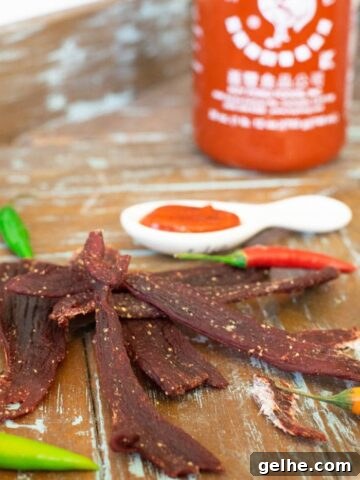 Sriracha Deer jerky on wood tray with sriracha bottle and peppers