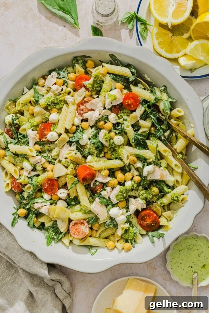Chicken pesto pasta salad tossed on a scalloped white bowl.