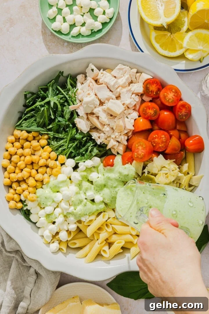 Creamy pesto dressing poured over pasta salad ingredients.