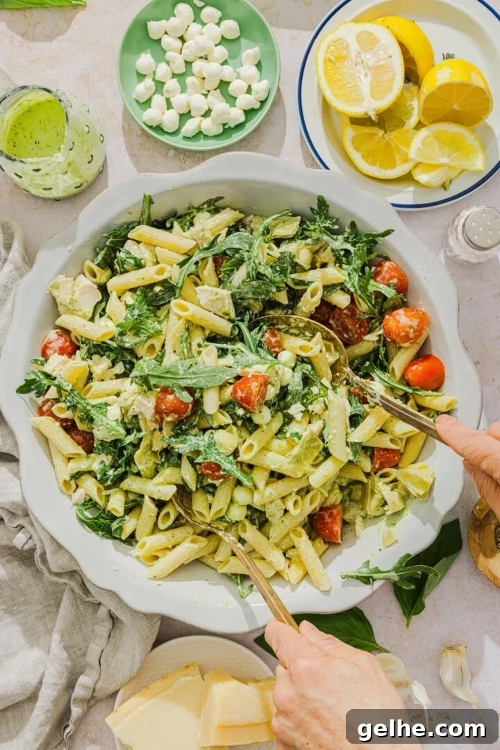 Creamy pesto pasta salad being tossed in a white bowl.