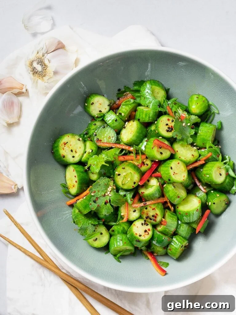 Spicy Asian cucumber salad with herbs and red pepper in a blue bowl next to garlic and chopsticks
