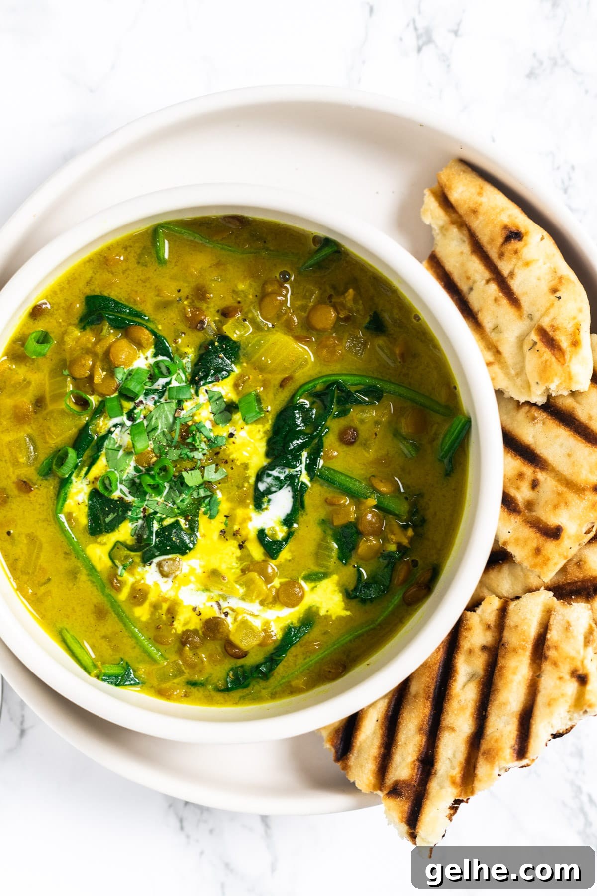 A top down view of a bowl of curried lentil soup with grilled naan bread on the side.