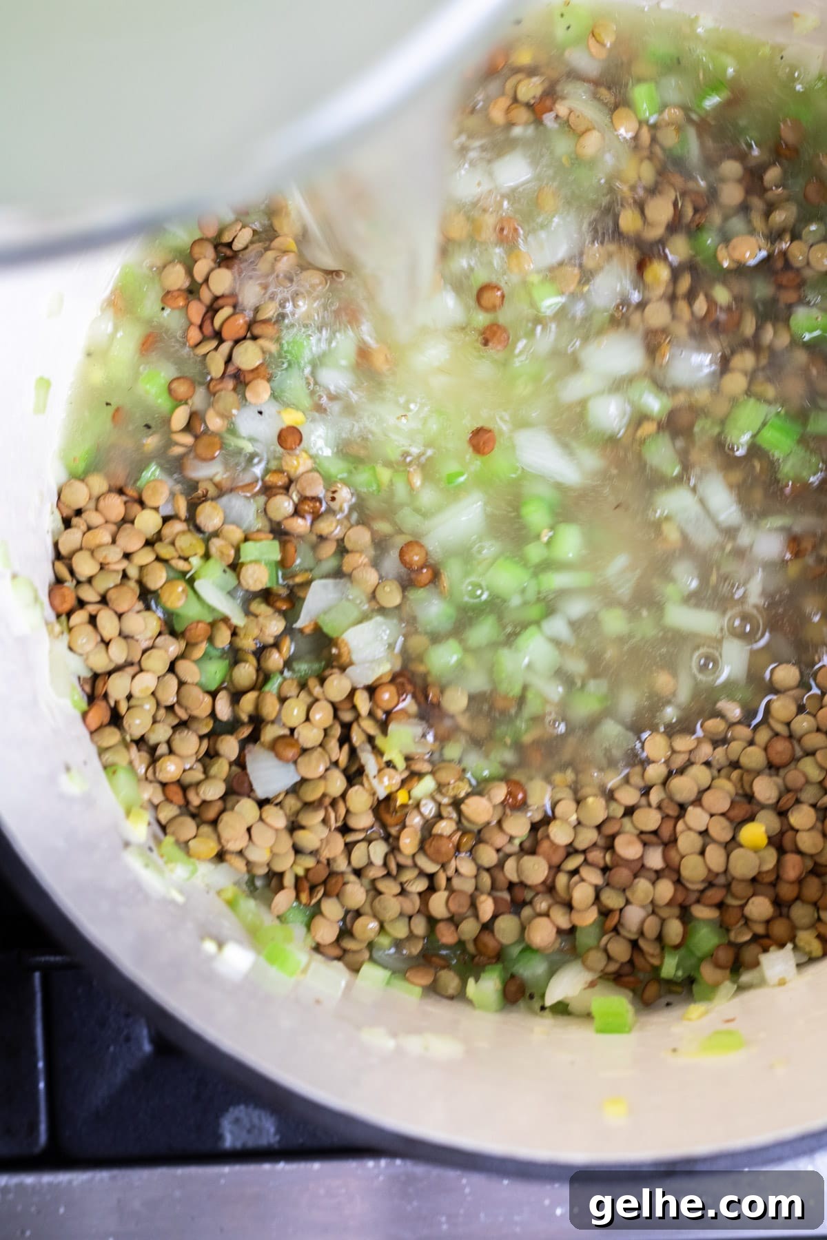 Pouring broth over the dried lentils and cooked veggies.