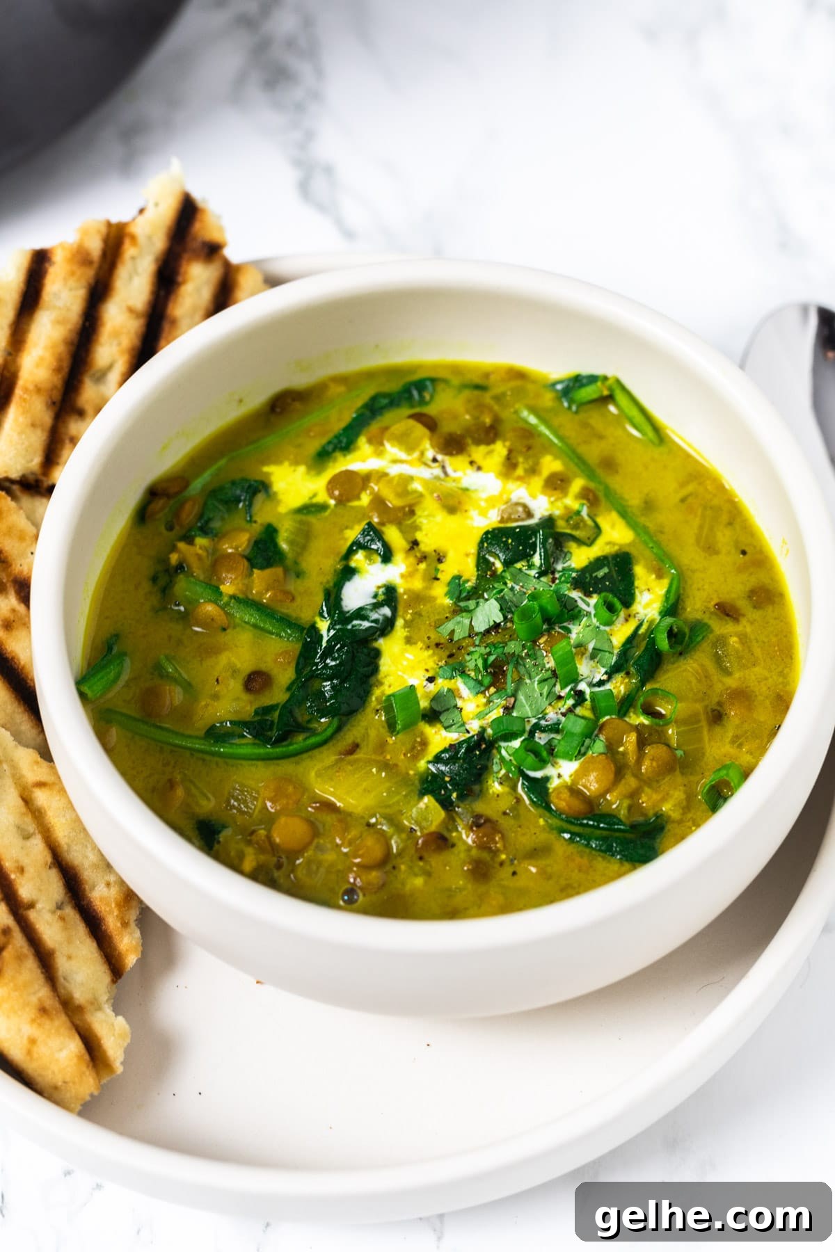 A side view of a bowl of curried lentil soup with a side of grilled naan bread.