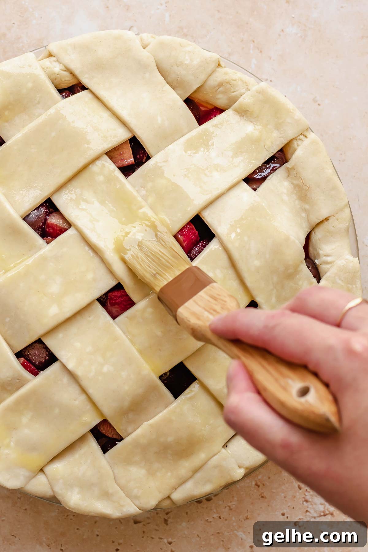 Cherry Rhubarb Pie Recipe: Sweet-Tart Homemade Dessert 14 A hand adds egg wash to the top of the lattice with a pastry brush.
