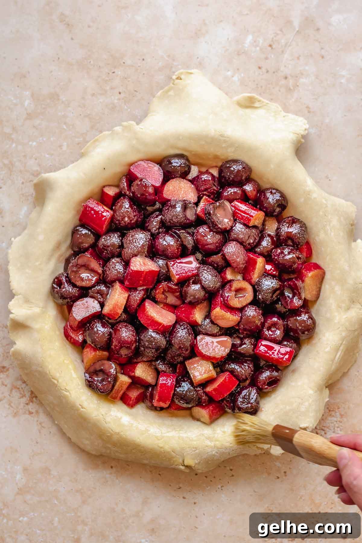 Cherry Rhubarb Pie Recipe: Sweet-Tart Homemade Dessert 10 Cherries and rhubarb in the center of the pie crust. A pastry brush adds egg wash to the edges.