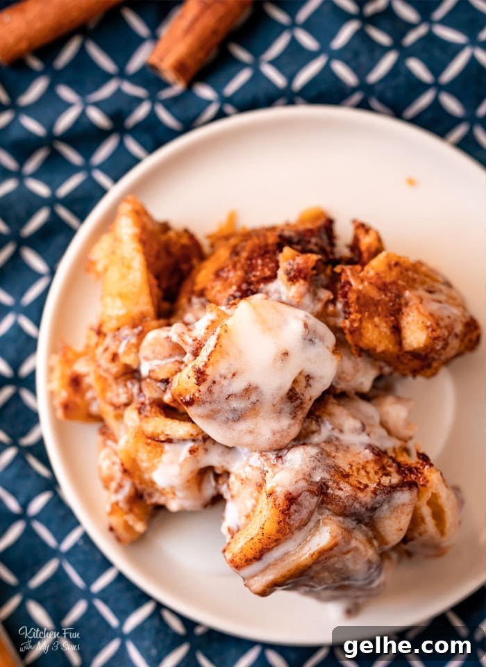 Overhead view of a serving of Crock Pot Cinnamon Roll Casserole on a white plate next to cinnamon sticks.