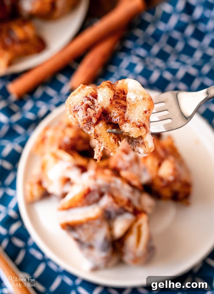 A forkful of Cinnamon Roll casserole held over a plate, with cinnamon sticks in the background.