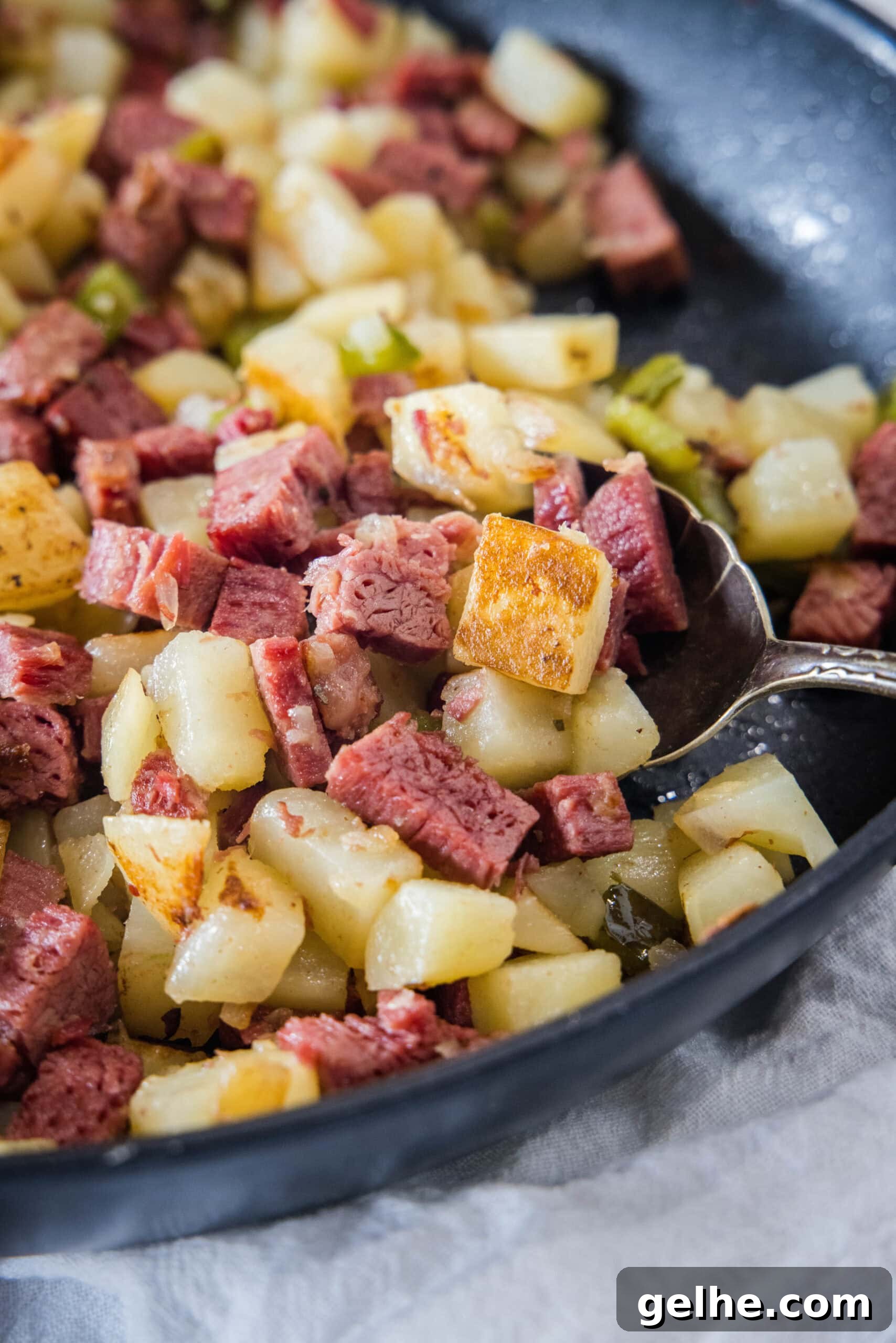 Make homemade corned beef hash with leftover corned beef, tender potatoes, onions, and bell peppers. An easy breakfast, ready in 30 minutes! Close up of corned beef hash in a skillet with a serving spoon.