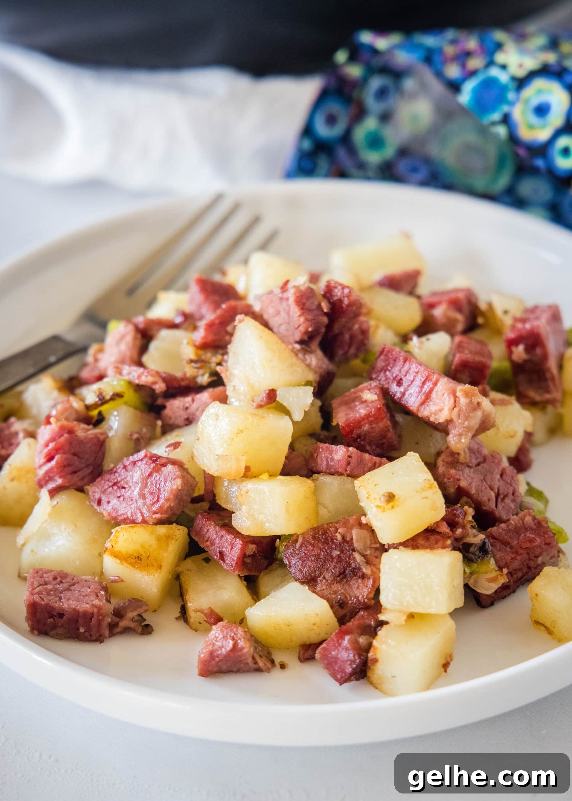 Make homemade corned beef hash with leftover corned beef, tender potatoes, onions, and bell peppers. An easy breakfast, ready in 30 minutes! A serving of corned beef hash on a white plate next to a fork.