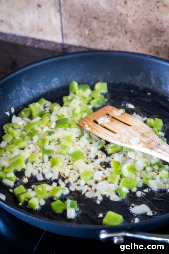 Make homemade corned beef hash with leftover corned beef, tender potatoes, onions, and bell peppers. An easy breakfast, ready in 30 minutes! Diced onions and bell pepper sauteing in a large skillet, with a wooden spatula.