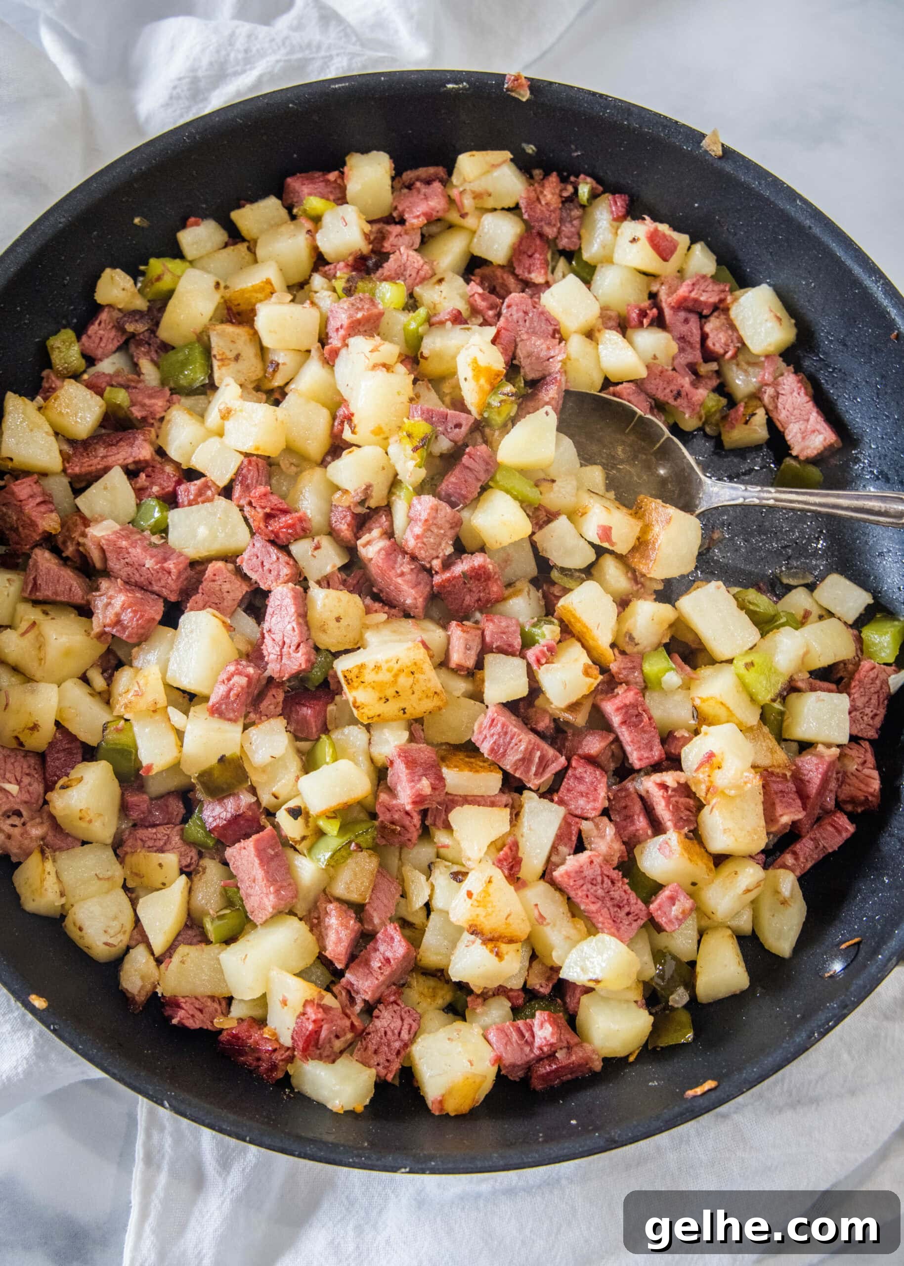 Make homemade corned beef hash with leftover corned beef, tender potatoes, onions, and bell peppers. An easy breakfast, ready in 30 minutes! Overhead view of corned beef hash in a large skillet with a serving spoon.