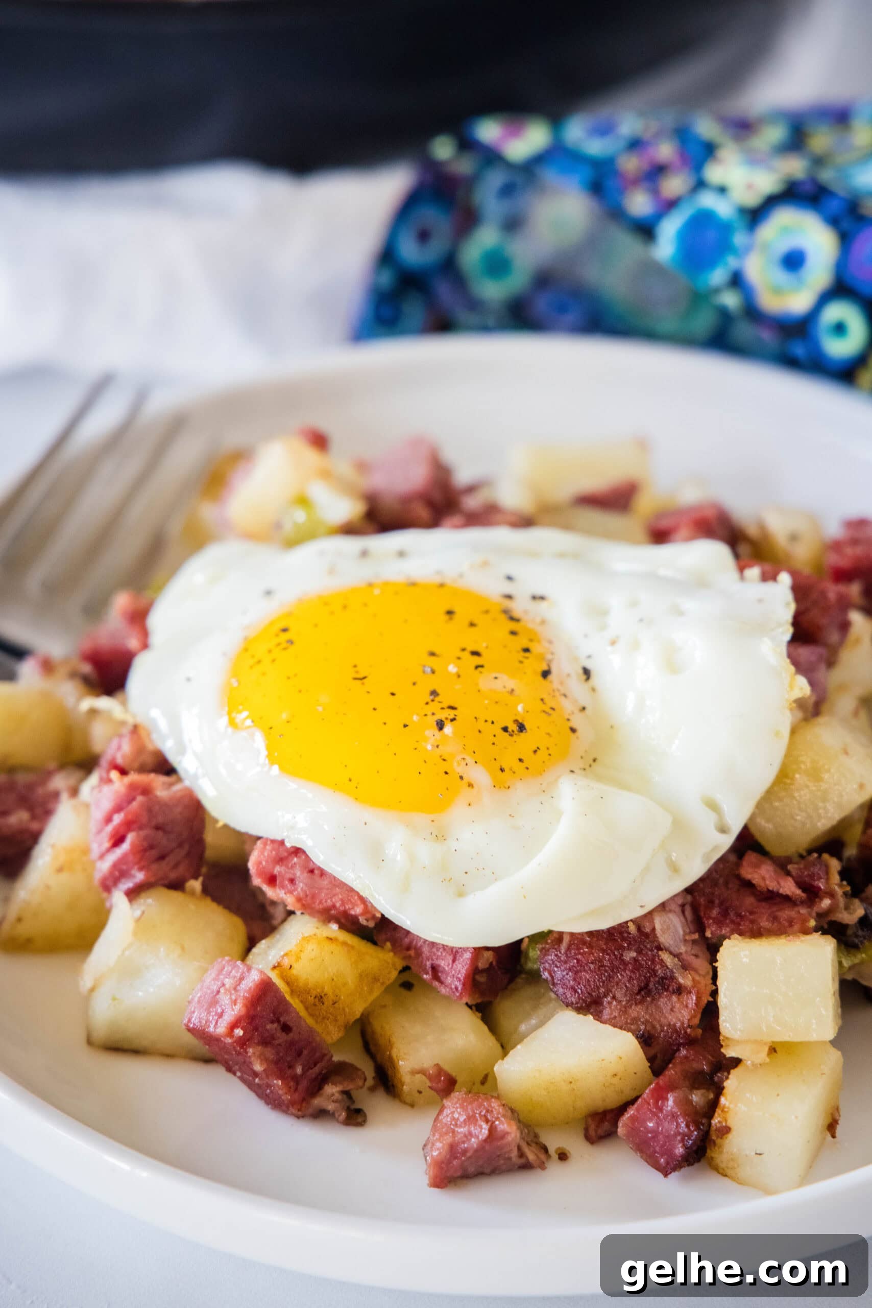 Make homemade corned beef hash with leftover corned beef, tender potatoes, onions, and bell peppers. An easy breakfast, ready in 30 minutes! Fried egg served over a bed of corned beef hash on a white plate.