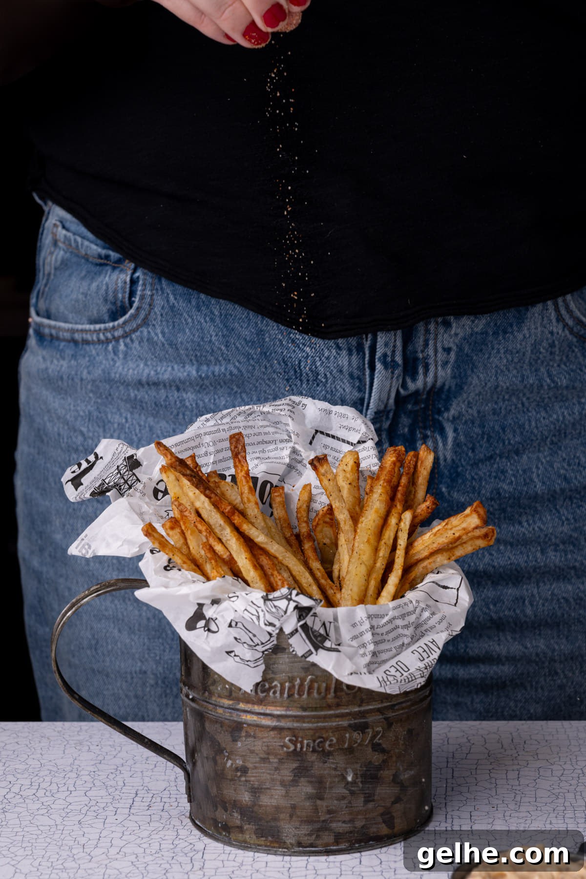 Crispy Cajun Fries: Oven or Air Fryer Recipe for Perfect Seasoning 2 Sprinkling hand cut homemade French fries with Cajun seasoning.
