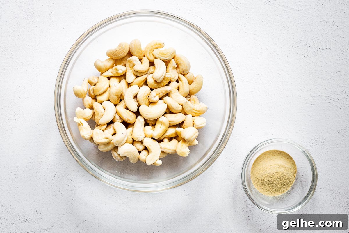 Soaked cashew nuts in a bowl next to a smaller glass bowl of nutritional yeast powder.