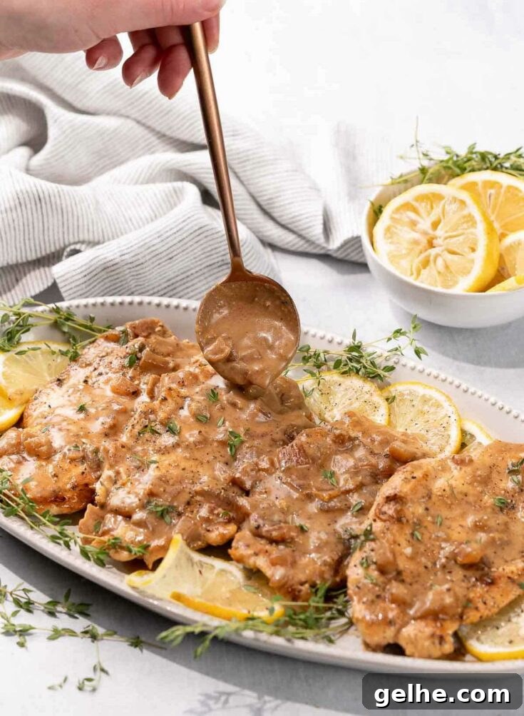 Lemon butter chicken on platter with herbs and lemon.