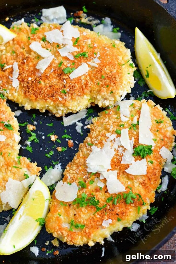 Chicken Milanese on black plate garnished with parsley and lemon.