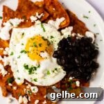 A close up view of a plate of red chilaquiles with black beans.