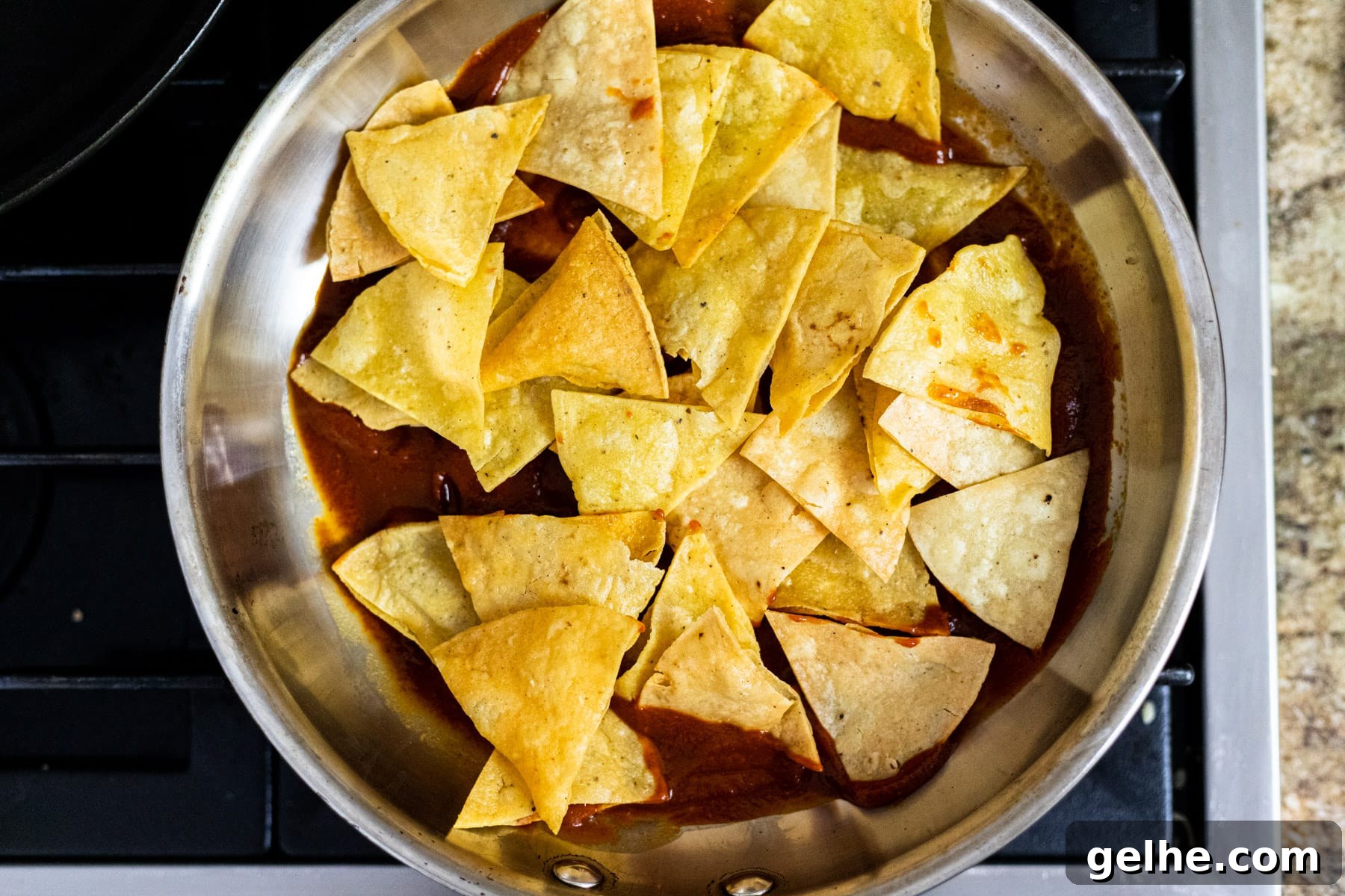 Tortilla chips on top of red chili sauce in a skillet.