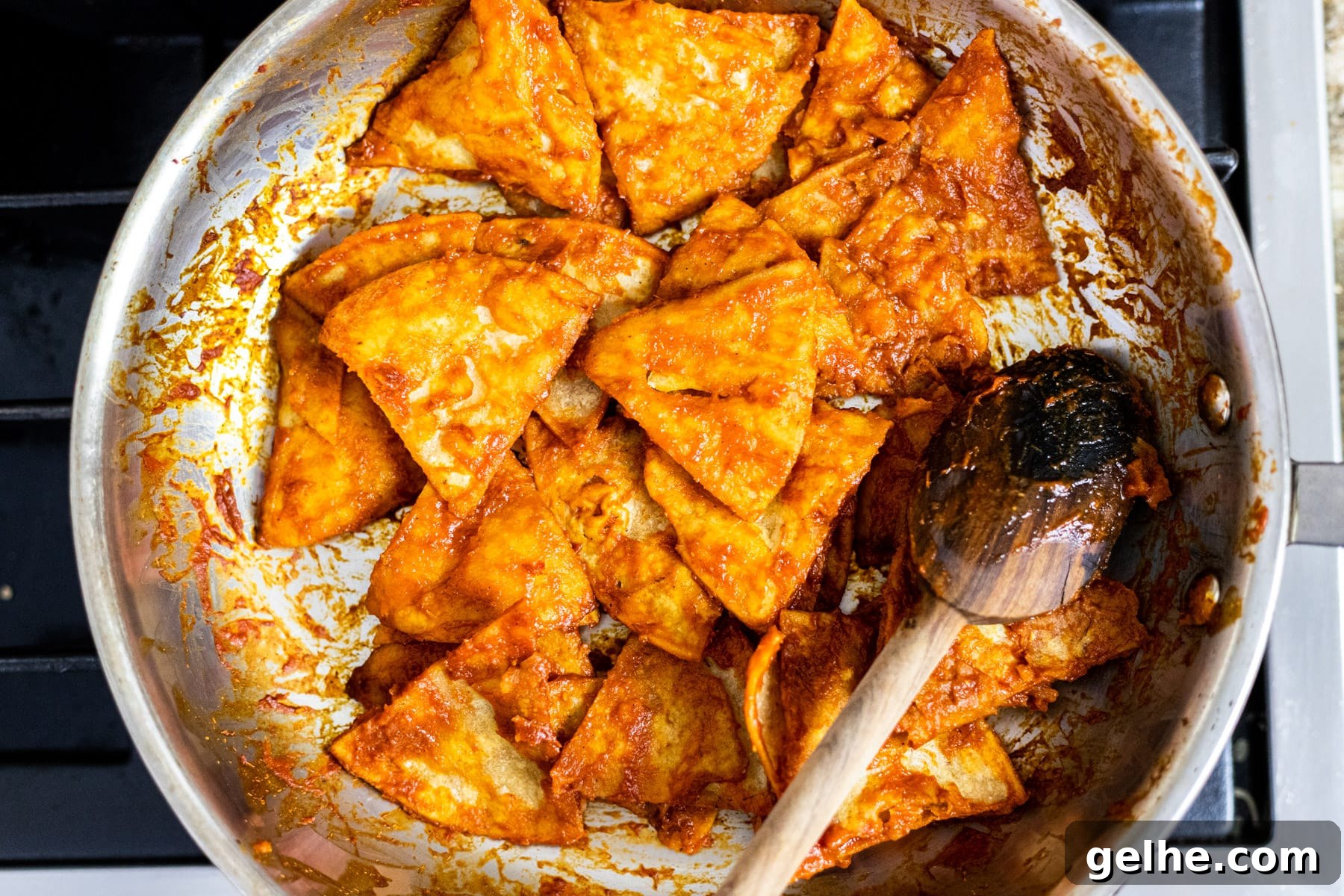 Tortillas covered in red chili sauce in a skillet.
