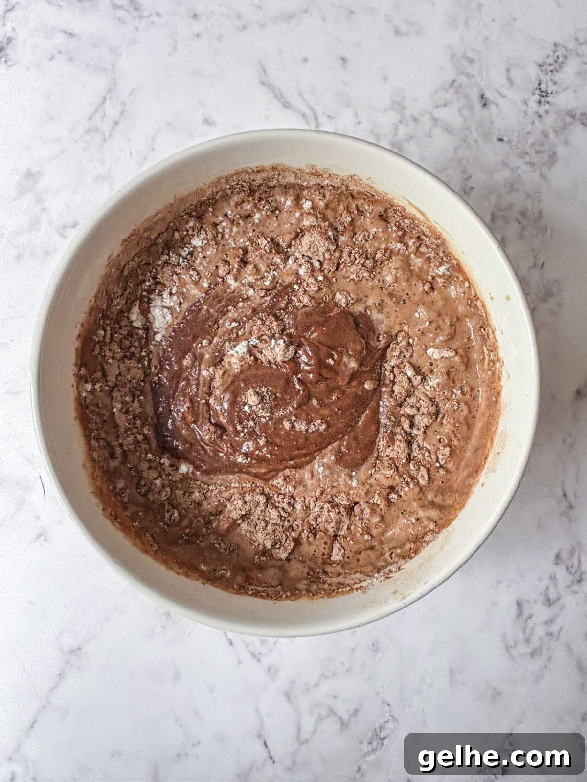 A white bowl filled with partially mixed chocolate cake batter.