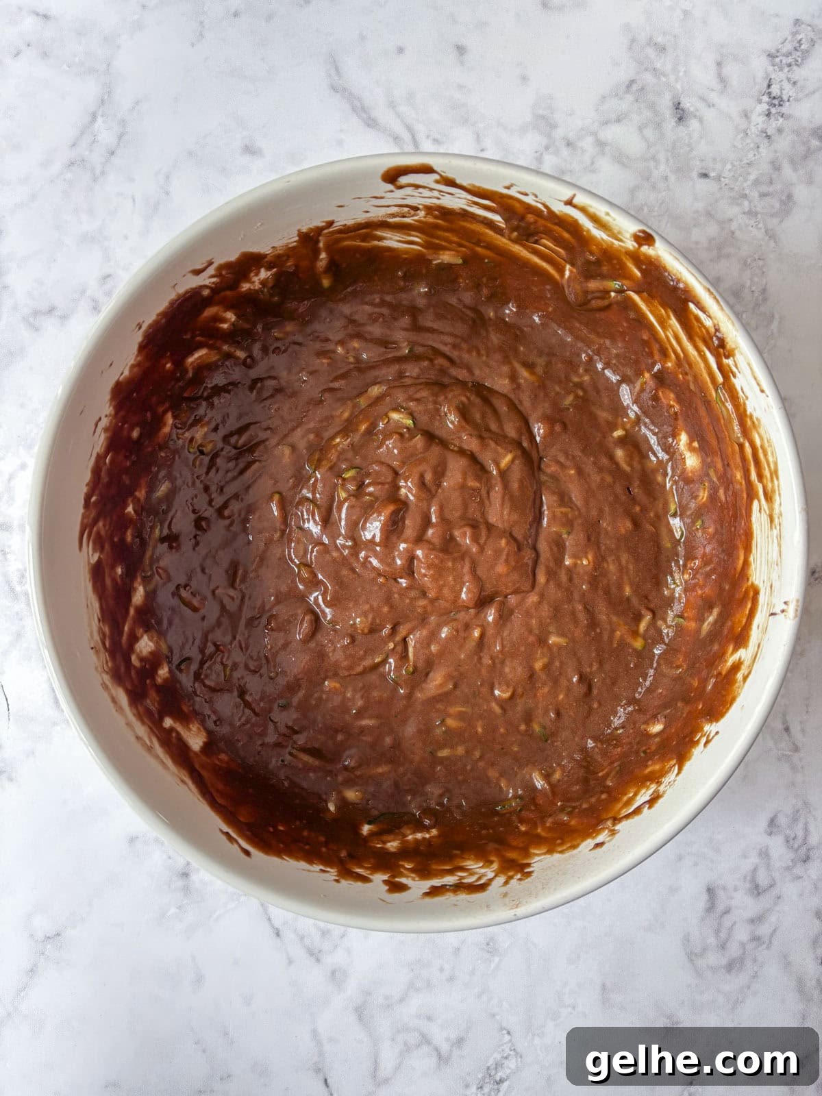 A white bowl filled with chocolate cake or brownie batter ready to be baked.
