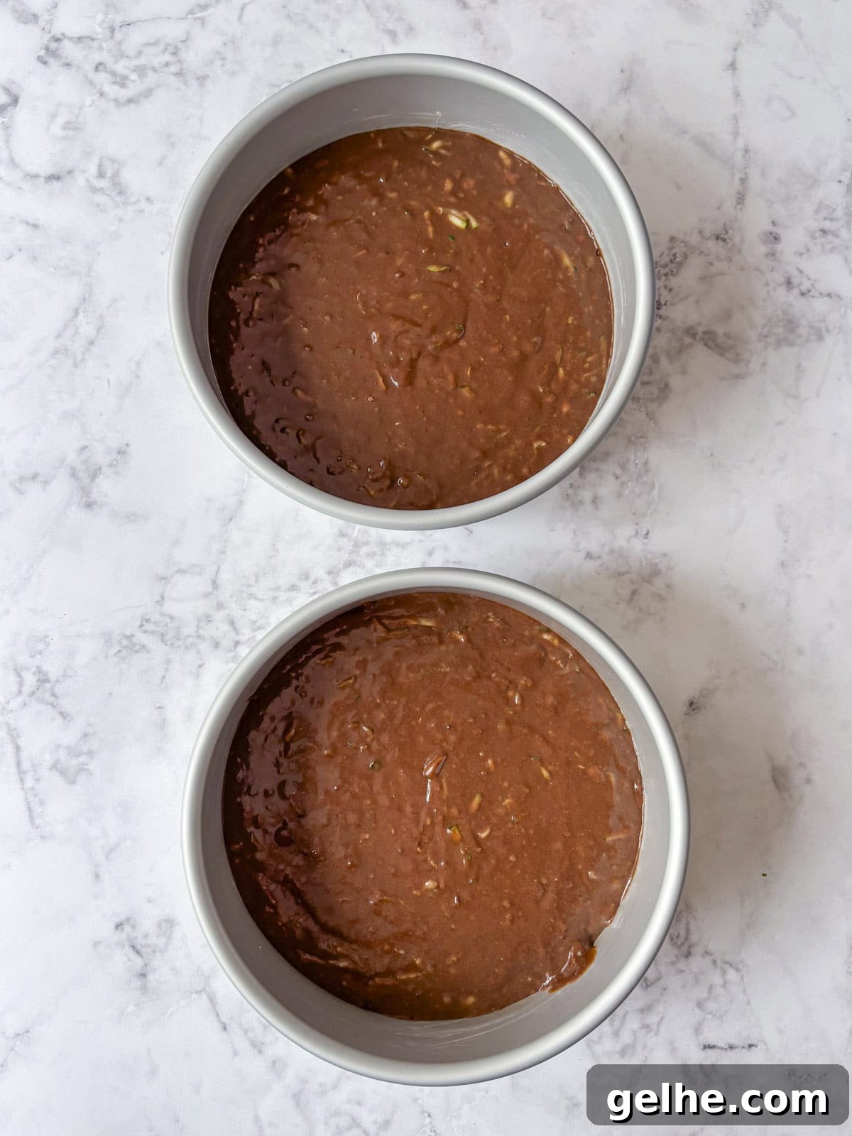 Two round cake pans filled with chocolate cake batter ready to be baked.