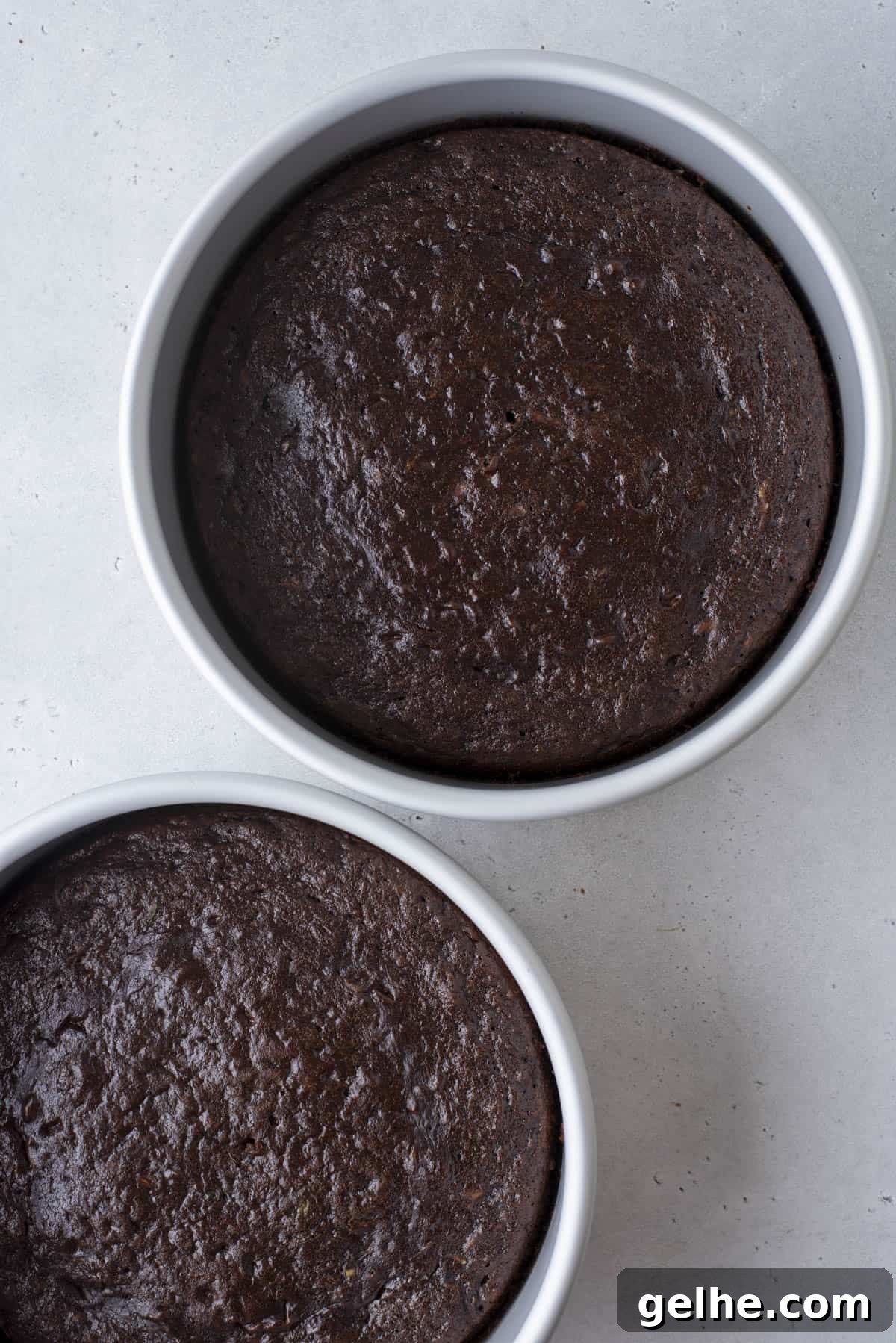 Two round cake pans filled with freshly baked chocolate cake, shown from above.