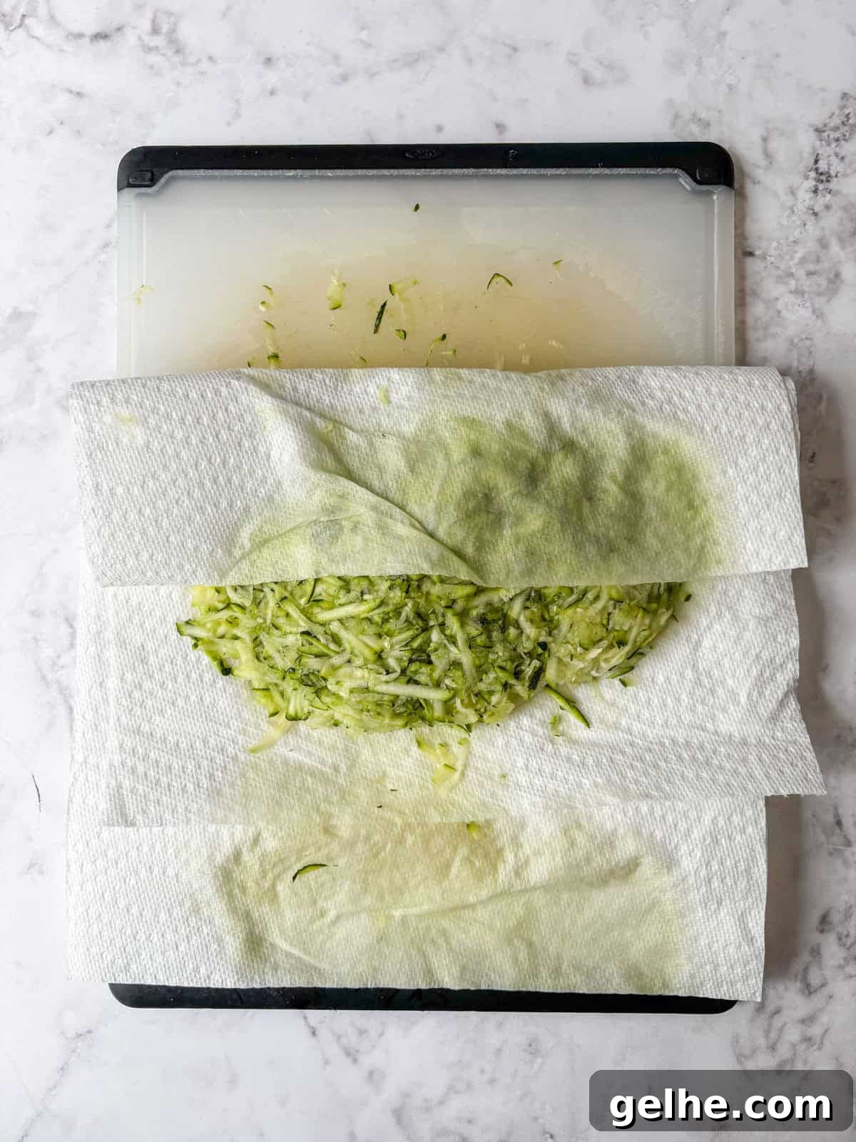 Shredded zucchini on a cutting board partially wrapped in paper towels with moisture absorbed into the towels.