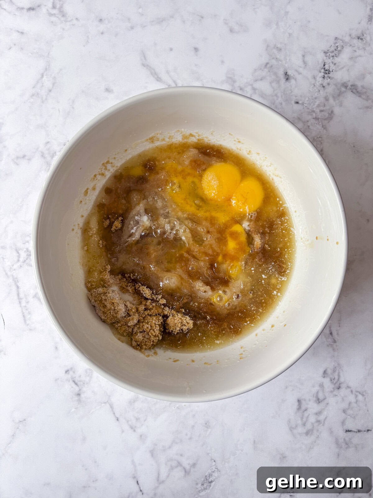 A white bowl containing eggs, brown sugar, and wet ingredients about to be mixed.