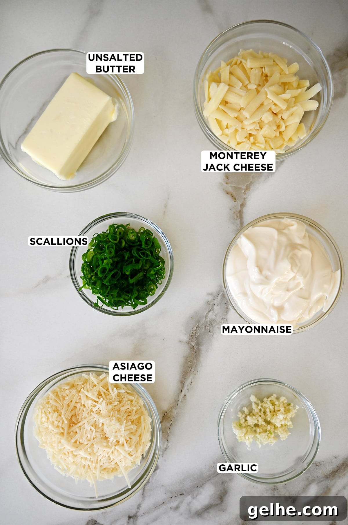 Glass bowls containing cheesy garlic bread ingredients, including butter, Monterey Jack cheese, mayonnaise, scallions, asiago cheese and minced garlic.
