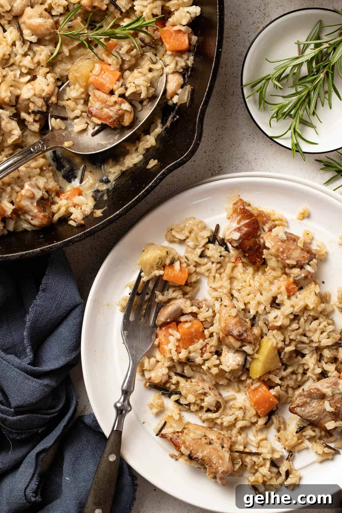 Dijon Chicken Skillet with Wild Rice and Creamy Mustard Sauce 10 Chicken and rice scooped onto a white plate next to fresh rosemary sprigs and a glass of water.