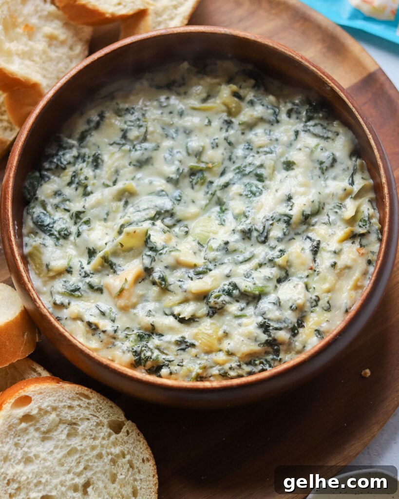 overhead view of a wooden bowl with homemade vegan spinach artichoke dip next to sliced bread.