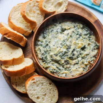 wooden bowl with warm vegan spinach and artichoke dip next to sliced pieces of bread.