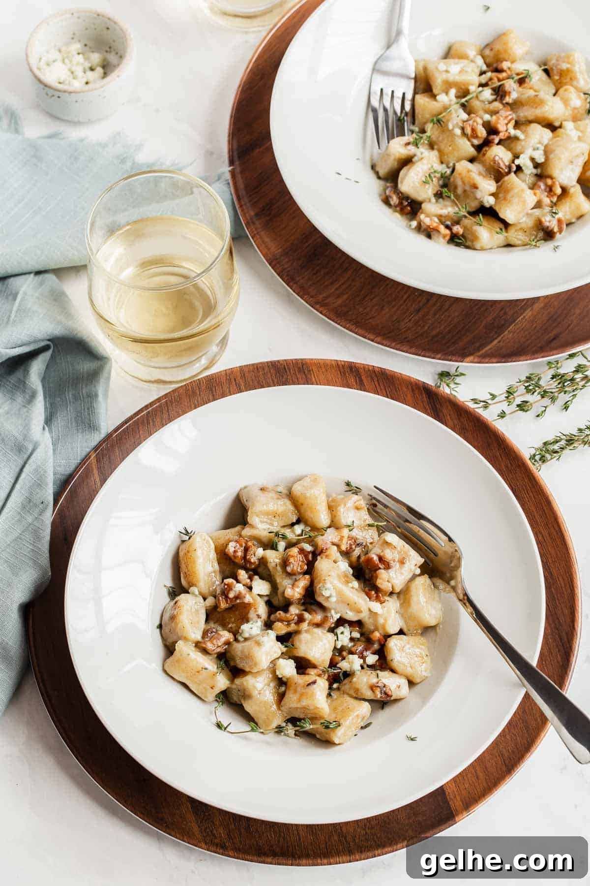Two serving plates of ricotta gnocchi with white wine on the side.