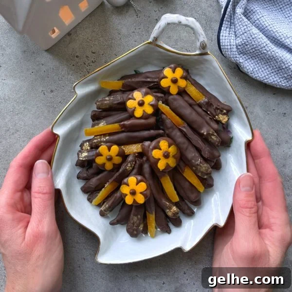A person holds a leaf-shaped plate filled with chocolate-dipped candied orange peels, decorated with small yellow flower-shaped chocolates.