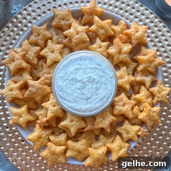 A plate of star-shaped Cheddar Crackers arranged neatly around a bowl of white dipping sauce.