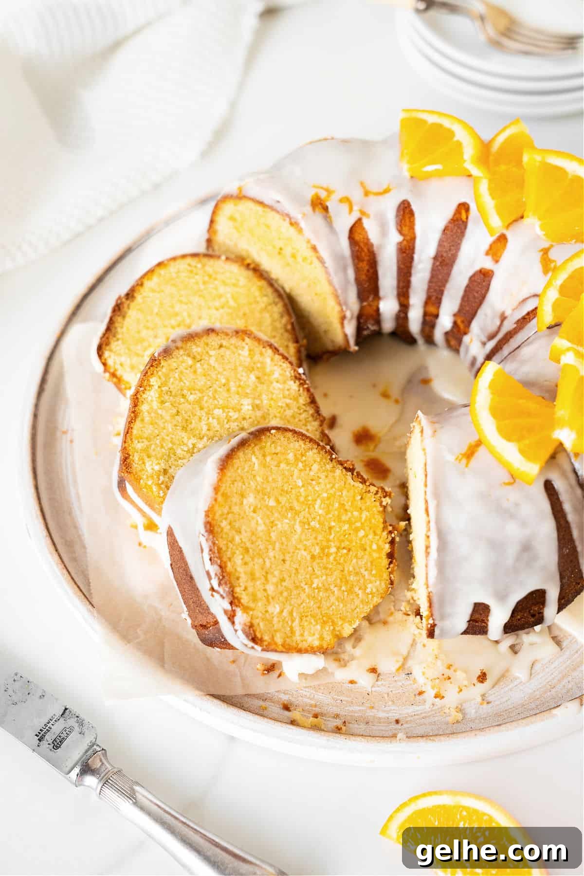 Sliced and whole glazed orange bundt cake on a white plate and white surface.
