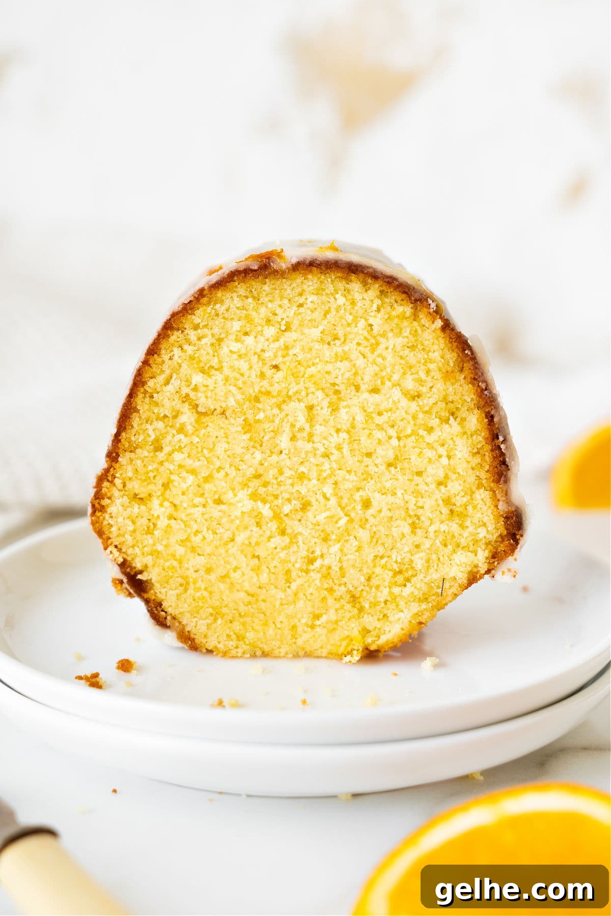 Single slice of glazed orange bundt cake on a white plate. White background.