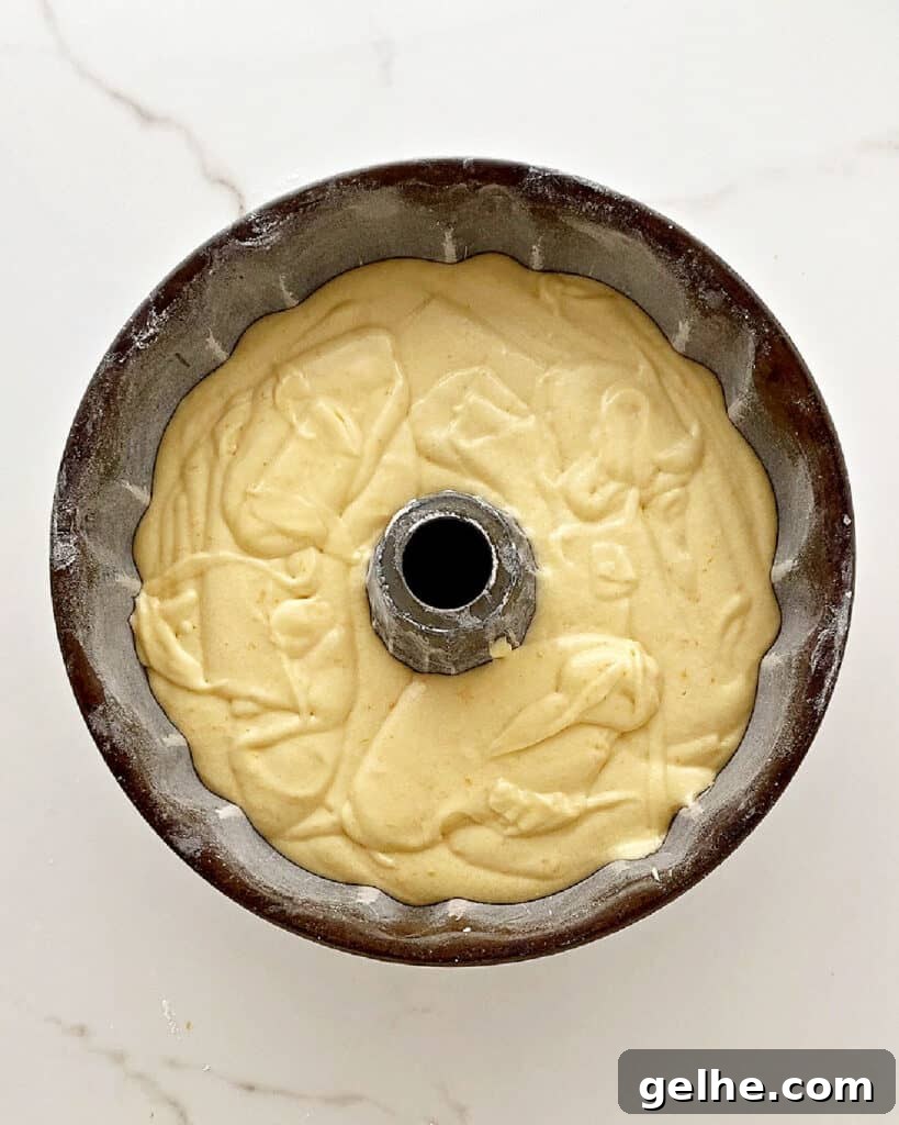Dark metal bundt pan with orange cake batter. White marbled surface. Top view.
