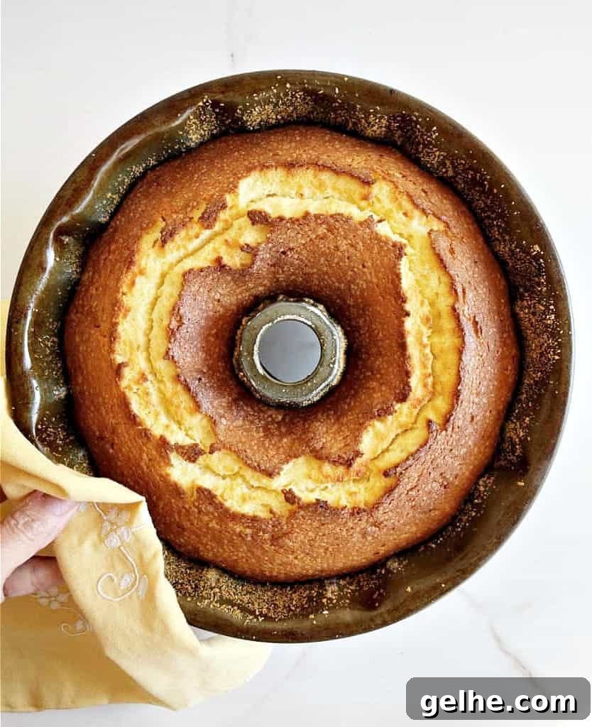 Whole baked orange cake in a dark bundt pan White surface. Top view.
