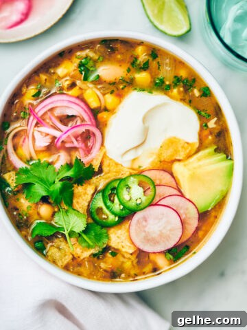 Vegan Green Chili Soup in a bowl with sour cream, pickled onions and cilantro.
