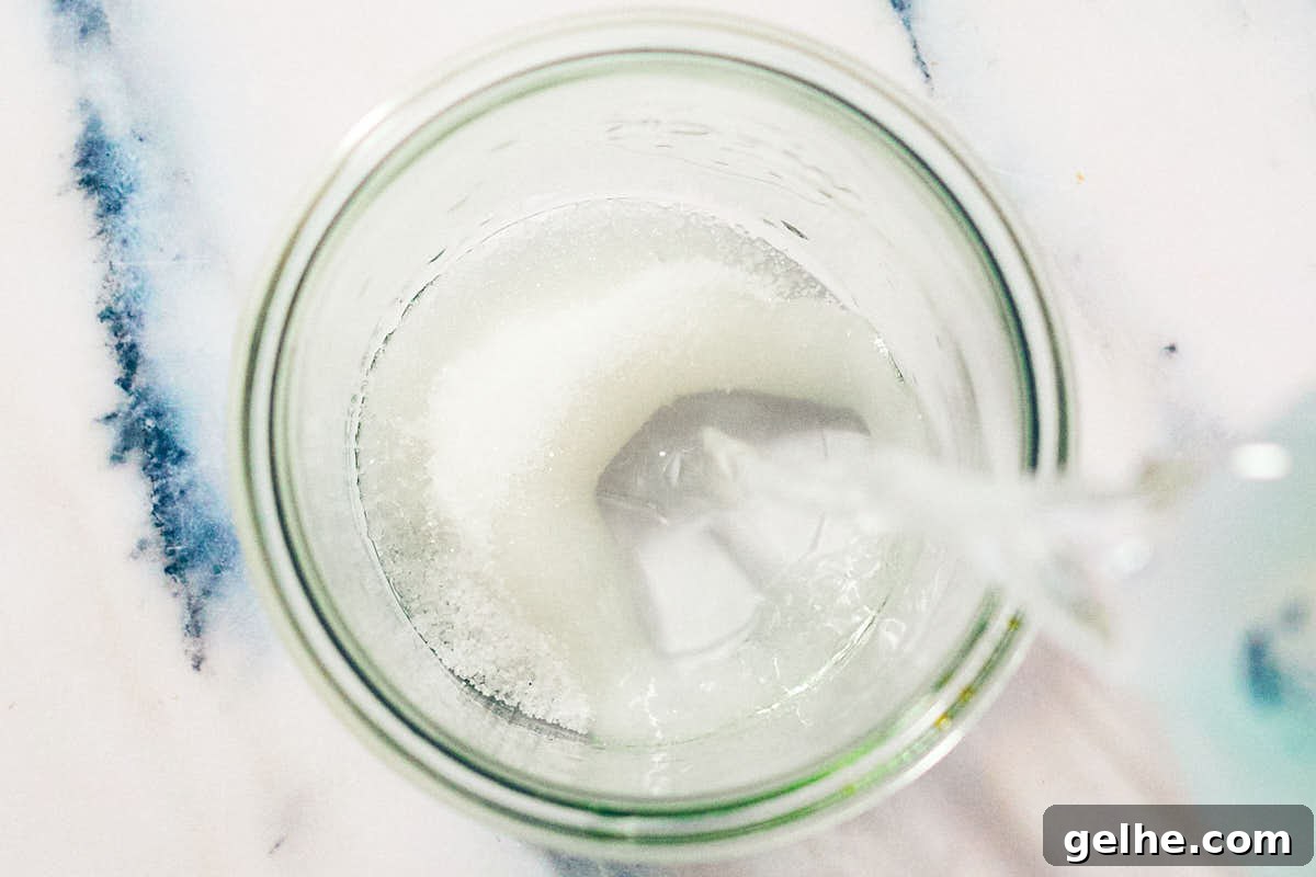 Hot water being poured into a glass jar with sugar and salt for pickling brine.