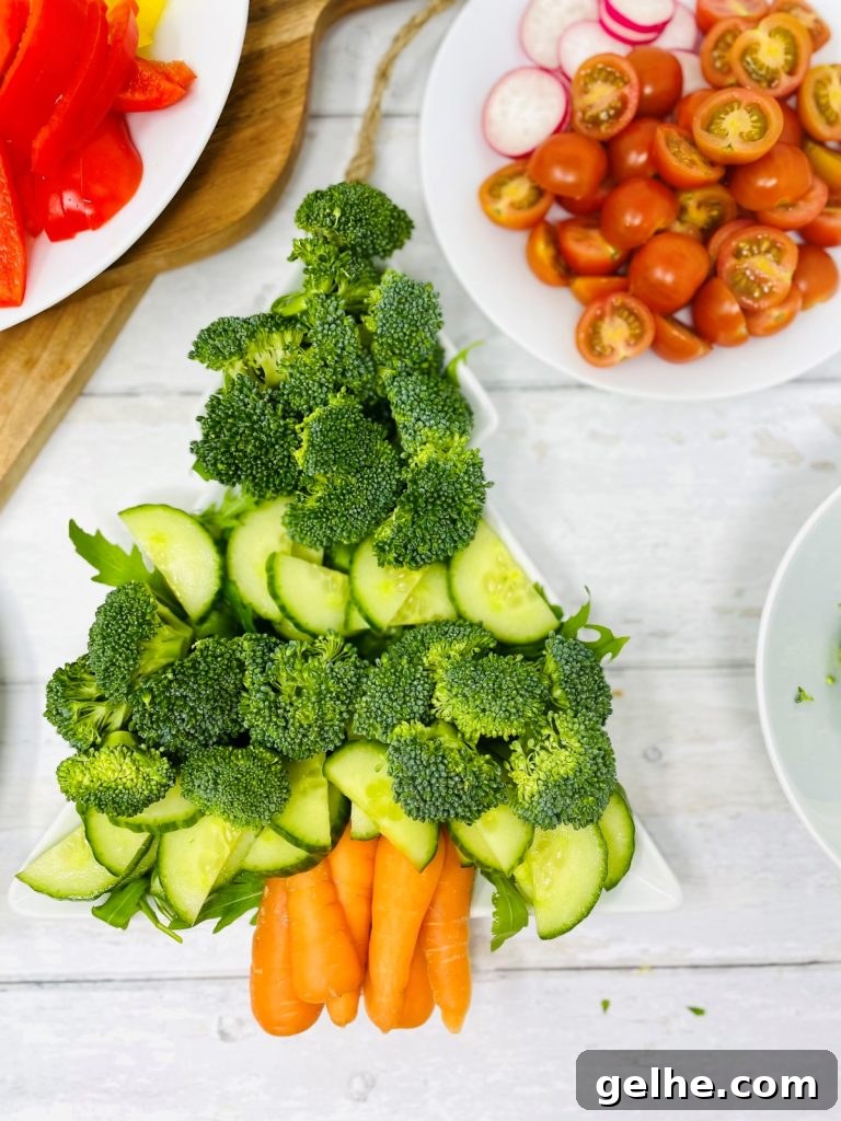 Image shows a christmas tree shaped plate with broccoli, cucumber, rocket and carrots on, there are also two other plates one with tomato and radish on and one with peppers on making up a crudité platter