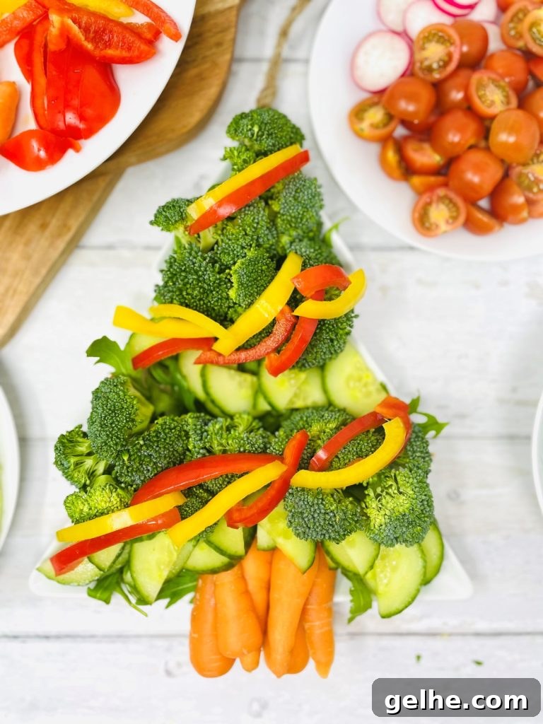 Image shows a christmas tree shaped plate with cucumber, peppers, broccoli, carrots and rocket, to the is a plate of tomatoes and radish making a crudité platter