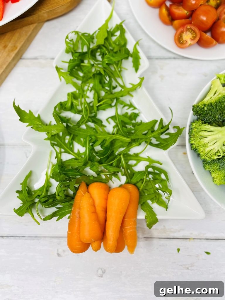 Image shows a christmas tree shaped plate with rocket scattered on it and carrots, next to a plate of broccoli, a plate of tomato and radish, a plate of peppers and a plate of cucumbers
