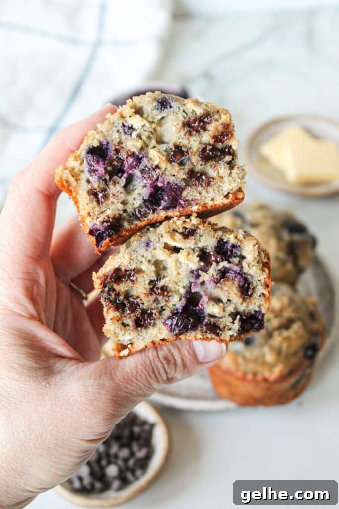 A hand holding two halves of a blueberry chocolate chip muffin, showing the inside.
