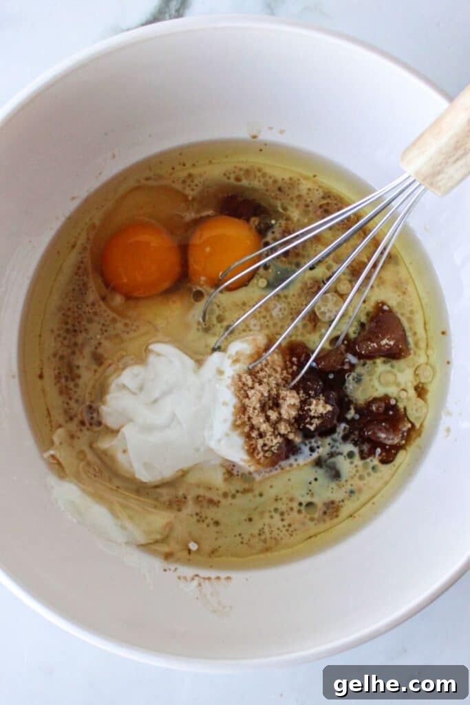 Wet ingredients for blueberry chocolate chip muffins in a white bowl with a whisk.