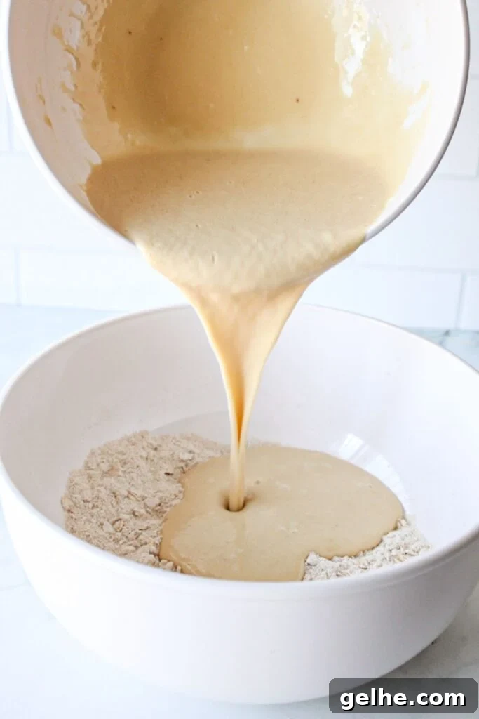 Blueberry chocolate chip muffin batter being poured into the bowl with dry ingredients.